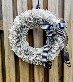 a wreath made out of old newspaper is hanging on a wooden fence with a black and white ribbon