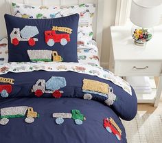 a child's bed with blue and white comforter, pillow cases and toy trucks on it