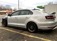 the rear end of a silver car parked in a parking lot next to a gas station