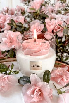 a candle that is sitting on a table with pink flowers in the background and greenery around it