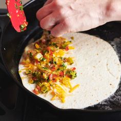 a tortilla being cooked in a skillet with vegetables and cheese on top