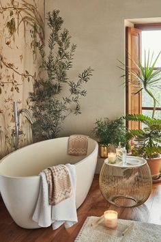 a bath tub sitting next to a window in a bathroom with plants on the wall