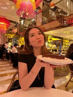 a woman sitting at a table holding a plate with a cake on it in front of her