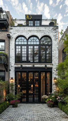 the entrance to a brick building with large arched windows and black doors, surrounded by greenery