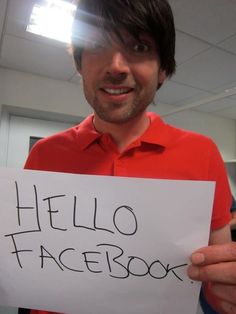 a man holding up a sign that says hello facebook