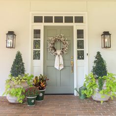 three potted plants sit in front of a door with a wreath hanging on it