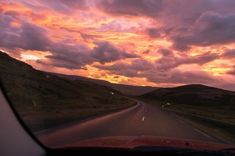 the sun is setting on an empty road with hills in the background and clouds above