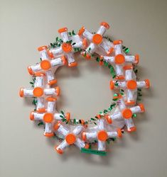 an orange and white wreath made out of plastic bottles is hanging on a gray wall