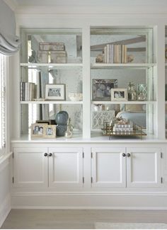 a white china cabinet with glass doors and shelves filled with books, pictures and other items