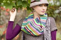 a woman wearing a knitted hat and scarf holding onto a leafy tree branch