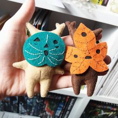 hand holding three small felt cat ornaments in front of bookshelves