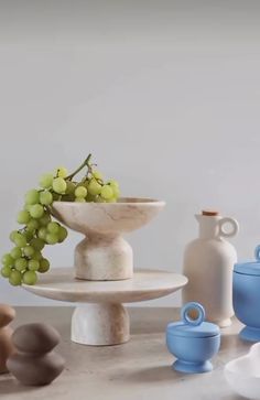 there are many different vases and bowls on the table, including one with grapes in it