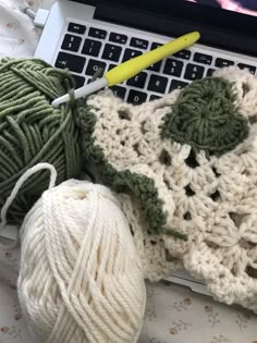 balls of yarn are sitting on top of a laptop computer and crochet is next to it