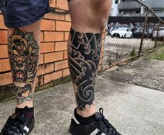 a man's legs with tattoos and sneakers on the ground next to a brick wall