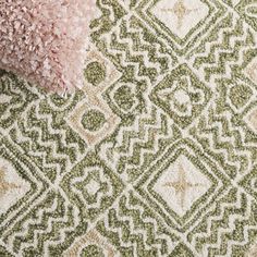 a green and white rug with a pink pillow on it's side next to a light pink throw pillow