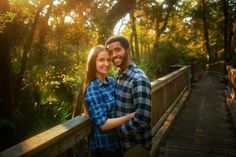 a man and woman are standing on a bridge in the woods with their arms around each other