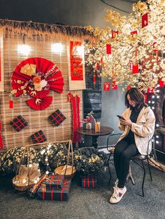 a woman sitting on a chair looking at her cell phone in front of some decorations