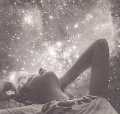 a woman laying on top of a bed under a sky filled with lots of stars