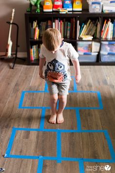 a toddler playing with blue tape on the floor in front of a bookshelf