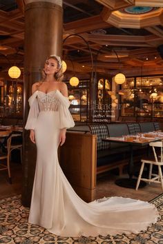 a woman standing in front of a table wearing a dress with an off the shoulder design