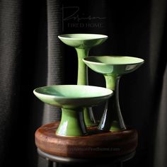 three green dishes sitting on top of a wooden stand in front of a black curtain