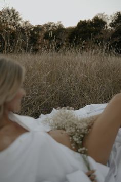 a woman laying on the ground with flowers in her hand and wearing a white dress