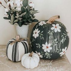 two painted pumpkins sitting on a table next to a vase with flowers in it