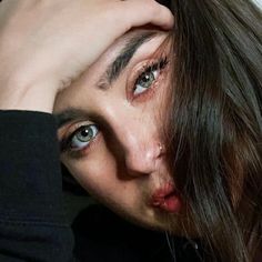 a close up of a person with long hair and blue eyes holding their hand on his head