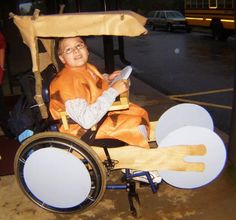 a young boy in an orange costume is riding on a small cart with wheels that are made out of plywood