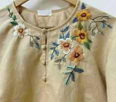 an embroidered shirt with flowers on it is hanging from a hanger and has buttons down the front