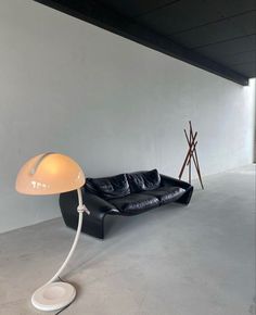 a black leather couch sitting next to a white lamp on top of a wooden stand