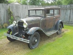 an old car is parked in the grass near a wooden fence and some trees,