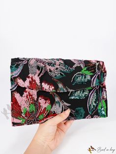 a hand holding a black and pink flowered clutch with green leaves on the front