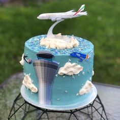 a blue cake with an airplane on top and clouds in the air is sitting on a stand