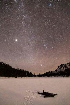 a person is laying in the snow with their feet up and looking at the stars above them