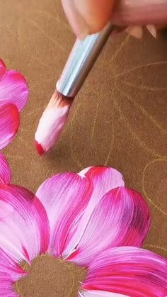 someone is painting flowers with pink paint on brown paper and using a pencil to draw the petals