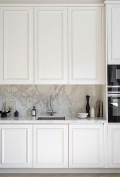 a kitchen with white cabinets and marble counter tops