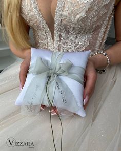 a woman in a wedding dress holding a white pillow with a silver bow on it