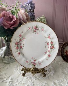 an antique china plate with pink and purple flowers in the center on a lace tablecloth