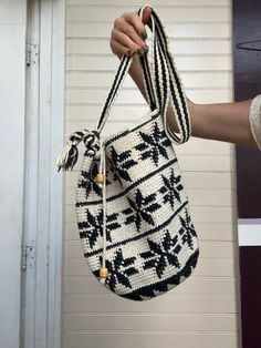 a hand holding a black and white knitted bag with tassels hanging from it