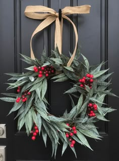 a wreath with red berries and green leaves hangs on the front door's black door