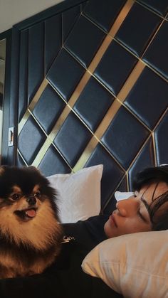 a woman laying in bed next to a dog on top of a pillow with her eyes closed