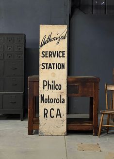 an old sign sitting on the ground next to a wooden table and chair in a room