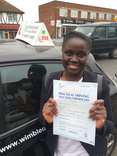 a woman holding up a driving certificate in front of a car