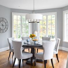 a dining room table with white chairs and a clock on the wall