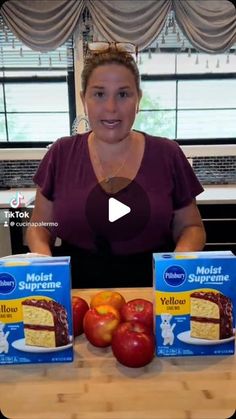 a woman sitting at a table with two boxes of cake mix and apples in front of her