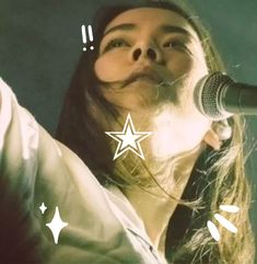 a woman singing into a microphone while holding her hand up in the air with an emoticive star above her head