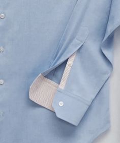 a blue shirt with white trim and buttons on the collar is laying flat against a white background