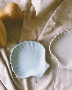 two white dishes sitting on top of a bed next to a banana and eggplant