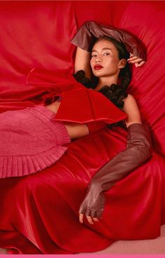 a woman laying on top of a red sheet in a pink dress and leather gloves